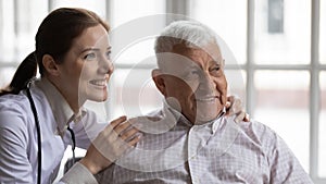 Young nurse hugs old man patient smiling look at distance photo