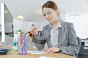 Young female office worker at computer desk sorting pencils