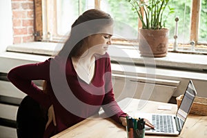 Young female office worker has back discomfort at work desk.