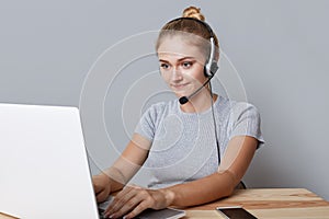Young female operator or consulatant has headphones, looks at laptop computer, makes video calls, uses high speed internet connect