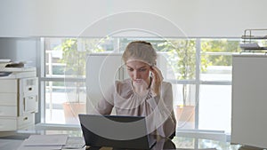 Young female operator wearing headset and talking with customer working on laptop in center office.