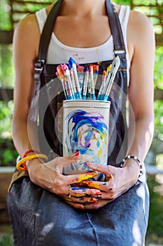 Young female painter artist holding a bunch of dirty used paintbrushes. Funky lifestyle creative hobbies background.