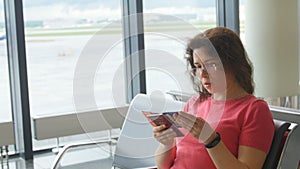 Young female passenger at the airport, using her phone while waiting for her flight