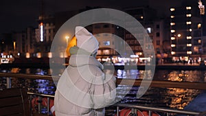 Young female passenger on boat passing by night embankment in sea city. Young girl tourist traveling by ship past night