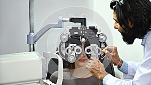 Young female patient checking eye vision with phoropter eyesight measurement testing machine in clinic