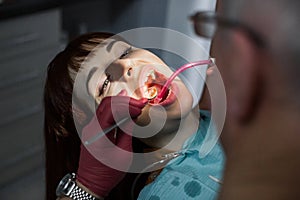 Young Female patient with open mouth having dental inspection and treatmant at dentist office. Senior man doctor dentist