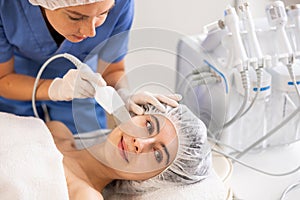 Young female patient undergoing facial skin cleansing with ultrasonic shovel