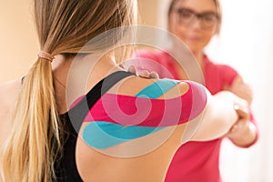 Young female patient wearing kinesio tape on her shoulder exercising with a professional physical therapist. Kinesiology.