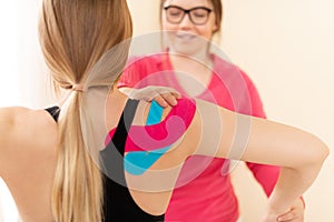 Young female patient wearing kinesio tape on her shoulder exercising with a professional physical therapist. Kinesiology.