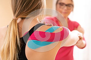 Young female patient wearing kinesio tape on her shoulder exercising with a professional physical therapist. Kinesiology. photo