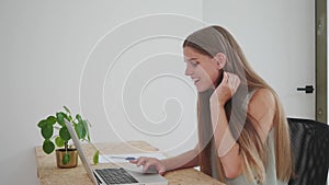 Young female person at the desk typing on her laptop having a positive reaction to a good news