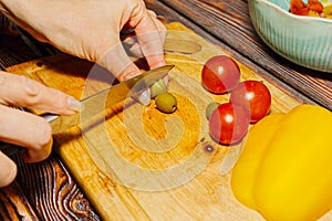 Young female person slicing green olives for salad