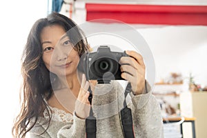 Young female photographer with a camera on a soft background taking pictures with her new camera