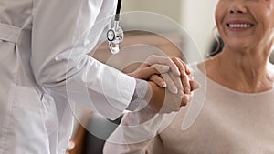 Young female physician holding hand of smiling elderly lady patient