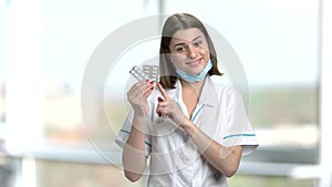 Young female physician holding pills.