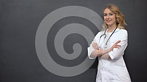 Young female physician posing near blackboard, template for medical advice