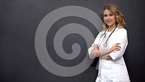 Young female physician posing near blackboard, template for medical advice