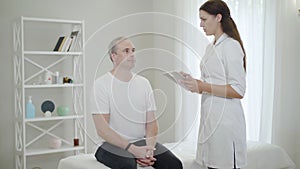 Young female physician taking medical history using tablet. Portrait of Caucasian doctor examining male patient in