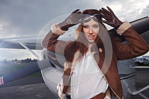 A young female pilot is standing next to a small training plane