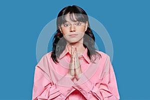 Young female pleading, holding hands in prayer request on blue background