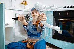 Young female plumber shows wrench and pipe