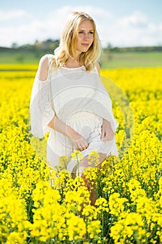 Young female posing in yellow oilseed rape field wearing in white dress