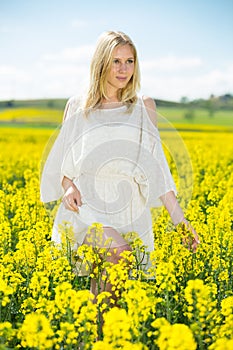 Young female posing in yellow oilseed rape field wearing in white dress