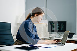 Young female programmer working with tablet and screen displaying code. Modern tech office setup, great for software, coding, IT
