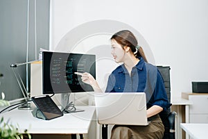 Young female programmer working with tablet and screen displaying code. Modern tech office setup, great for software, coding, IT