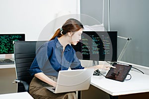 Young female programmer working with tablet and screen displaying code. Modern tech office setup, great for software, coding, IT
