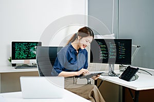 Young female programmer working with tablet and screen displaying code. Modern tech office setup, great for software, coding, IT