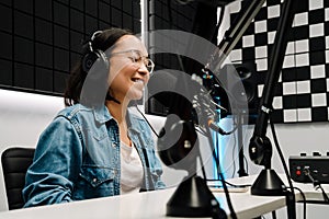 Young female radio host using microphone and headphones in studio