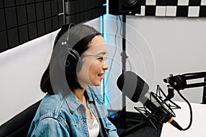 Young female radio host using microphone and headphones in studio