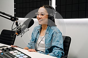 Young female radio host using microphone and headphones in studio