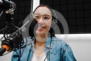 Young female radio host using microphone and headphones in studio