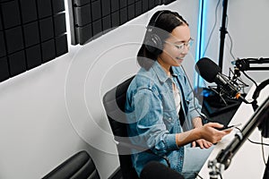 Young female radio host using microphone and headphones in studio