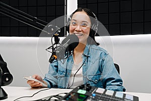 Young female radio host using microphone and headphones in studio