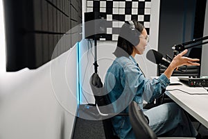 Young female radio host using microphone and headphones in studio