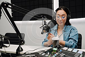 Young female radio host using microphone and headphones in studio