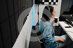 Young female radio host using microphone and headphones in studio