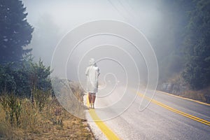 Young female in a raincoat on the road in the fog. Travel of women in the raincoat hitchhiking in the rain