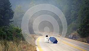 Young female in a raincoat and umbrella on the road in the fog. Travel of women in the raincoat hitchhiking in the rain