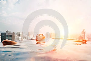 Young female relaxing in top roof infinity swimming pool with city view to the modern business center downtown with a skyscrapers