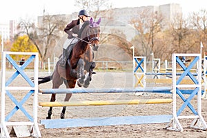 Young female rider on bay horse jump over hurdle