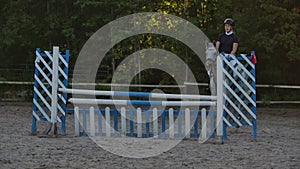 Young female rider on bay horse jumping over hurdle on equestrian sport competition.