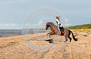 Young female rider is enjoying a leisurely moment astride a brown horse on a beach