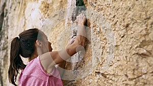 Young female rock climber trying to climb on a cliff, searching, reaching and gripping hold.