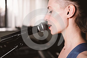 young female rock singer with microphone, singing. side view. close up. woman with short hair on a stage. live music