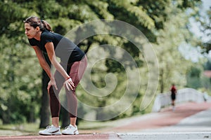 Young female runner catching her breath after a run in a park