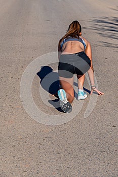Young female runner, crouched in a starting position, prepared to sprint and run on an asphalt athletics track or road with her